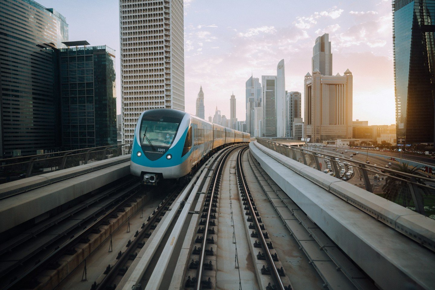 Dubai Metro train on an elevated track with the Dubai skyline at sunset